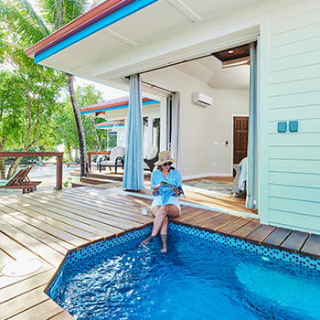 a girl reading a book while dipping her feet in the private pool at ray caye resort suite